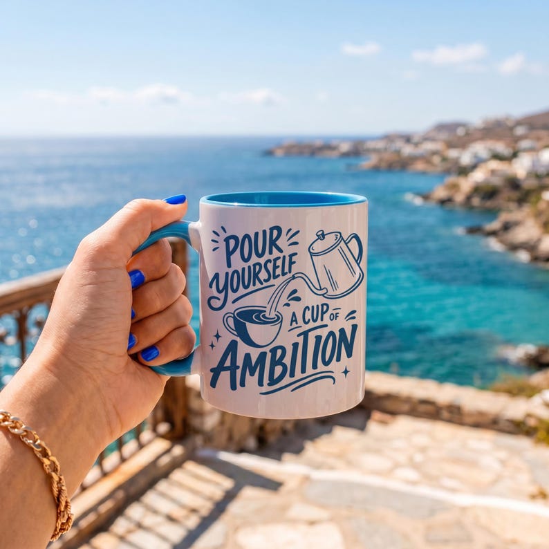 Puede incluir: Una taza de cer&aacute;mica blanca con interior y asa de color azul brillante. El exterior presenta un texto en azul oscuro que dice "POUR YOURSELF A CUP OF AMBITION" junto a una ilustraci&oacute;n gr&aacute;fica de una cafetera vertiendo l&iacute;quido.