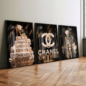 Könnte beinhalten: Drei rechteckige Wandkunstdrucke mit schwarzem Marmorhintergrund. Der erste zeigt gestapelte Bücher mit den Aufschriften Burberry, Chanel, Prada und Gucci sowie einen Stöckelschuh. Der zweite zeigt ein großes Chanel-Logo. Der dritte zeigt Parfümflakons.