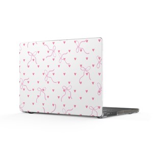 May include: A laptop with a white hard shell case featuring a repeating pattern of small pink hearts and light pink ribbon bows. The design covers the entire back of the laptop lid, displaying a consistent motif of delicate hand-drawn style bows.