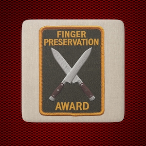 May include: A square patch with a dark gray background and a gold border. The text FINGER PRESERVATION AWARD is embroidered in gold. Two silver chef knives with dark red handles are crossed in the center, featuring detailed white stitching.