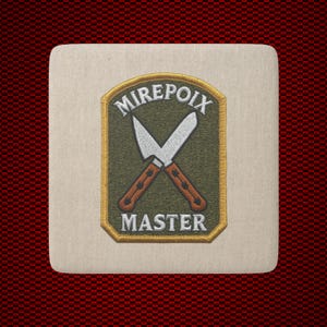 May include: A square off-white coaster featuring an embroidered patch with an olive green background. The patch displays two crossed silver knives with brown handles, surrounded by a gold border, with the text MIREPOIX above and MASTER below.