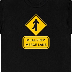 Könnte beinhalten: Ein schwarzes T-Shirt mit einer gelben, rautenförmigen Verkehrsschild-Grafik, die einen schwarzen Einfädelungspfeil zeigt. Unter der Raute befindet sich ein gelbes, rechteckiges Schild mit dem schwarzen Text MEAL PREP MERGE LANE.