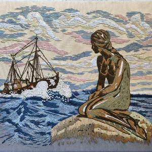 May include: A detailed embroidery on fabric depicting a figure sitting on a rock in the foreground, looking toward a fishing boat navigating choppy blue ocean waves. The sky features soft pink, white, and blue clouds above the sea scene.