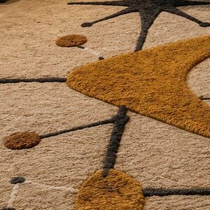 May include: A textured area rug featuring a beige background with a repeating pattern of dark gray lines, mustard yellow boomerang shapes, and small circular accents in both mustard yellow and dark gray, creating a geometric, mid-century inspired design.