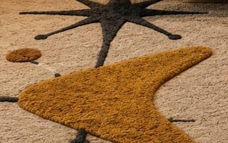 May include: A textured area rug featuring a cream-colored background with a large, dark charcoal starburst shape and a prominent, mustard-yellow boomerang-shaped design. The surface has a thick, tufted pile with visible loops and varied yarn textures.