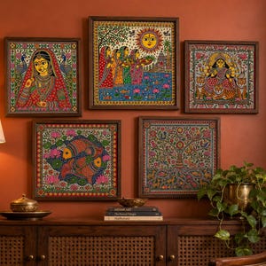 May include: A collection of five square framed wall art pieces featuring intricate Madhubani style paintings. The artworks depict a woman in traditional attire, figures near a sun, a deity on tigers, two fish, and a tree of life, all in vibrant colors.