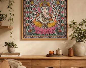 Może przedstawiać: Kwadratowy obraz w ramie przedstawiający kolorową ilustrację hinduskiego bóstwa Ganesha siedzącego na różowym kwiecie lotusa, w towarzystwie dwóch małych szarych myszy, zamknięty w ozdobnej kwiatowej ramce z misternymi wzorami.