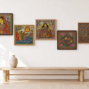 May include: A set of five square framed wall art pieces featuring intricate, colorful Indian folk art illustrations. The prints depict a woman in traditional attire, a sun scene with figures, a multi-armed deity on a tiger, a floral motif, and a tree.