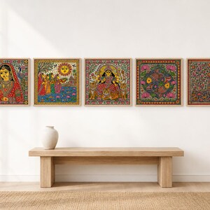 May include: A set of five square wall art prints featuring intricate, colorful folk-style illustrations. The designs depict a woman in traditional attire, a group of figures under a sun, a multi-armed deity with tigers, two fish, and a tree of life.