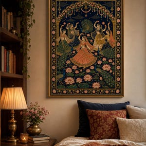 May include: A rectangular framed wall art print featuring a dark blue background with five figures in traditional attire dancing amidst pink lotus flowers and peacocks. The scene is framed by an ornate floral border with a gold-colored frame.