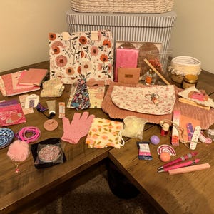May include: A collection of assorted items including a floral tote bag, pink exfoliating gloves, a patterned pouch, notebooks, pens, a small ceramic dish, a compact mirror, hair accessories, skincare products, and various small decorative trinkets.