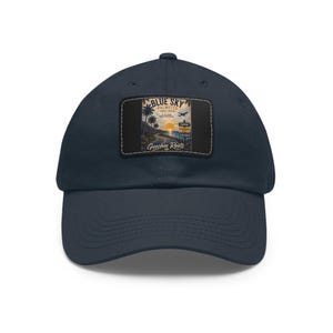 May include: A navy blue baseball cap featuring a rectangular patch on the front. The patch displays a coastal scene with palm trees, a sunset, an airplane, and a road sign. The text on the patch reads Blue Sky Palmetto, Geechee Roots.