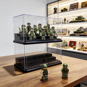 May include: A clear acrylic two-tier display case with black stepped risers designed for minifigures. The case contains ten military-themed plastic figures in green uniforms and helmets, with two additional matching figures standing in front.