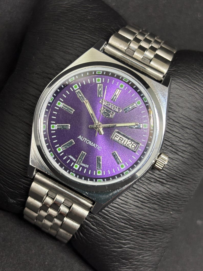 Peut inclure: Une montre-bracelet automatique Seiko 5 argent&eacute;e dot&eacute;e d'un cadran violet &eacute;clatant &agrave; effet rayon de soleil, avec des index rectangulaires, des aiguilles luminescentes et un guichet jour-date &agrave; trois heures. Bracelet &agrave; maillons en acier.