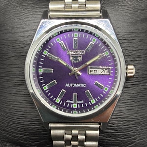 Peut inclure: Une montre-bracelet automatique en acier inoxydable argent&eacute; dot&eacute;e d'un cadran violet vif &agrave; effet soleil avec des index b&acirc;tons argent&eacute;s, des aiguilles luminescentes et un guichet jour-date &agrave; trois heures. Bracelet &agrave; maillons en m&eacute;tal.