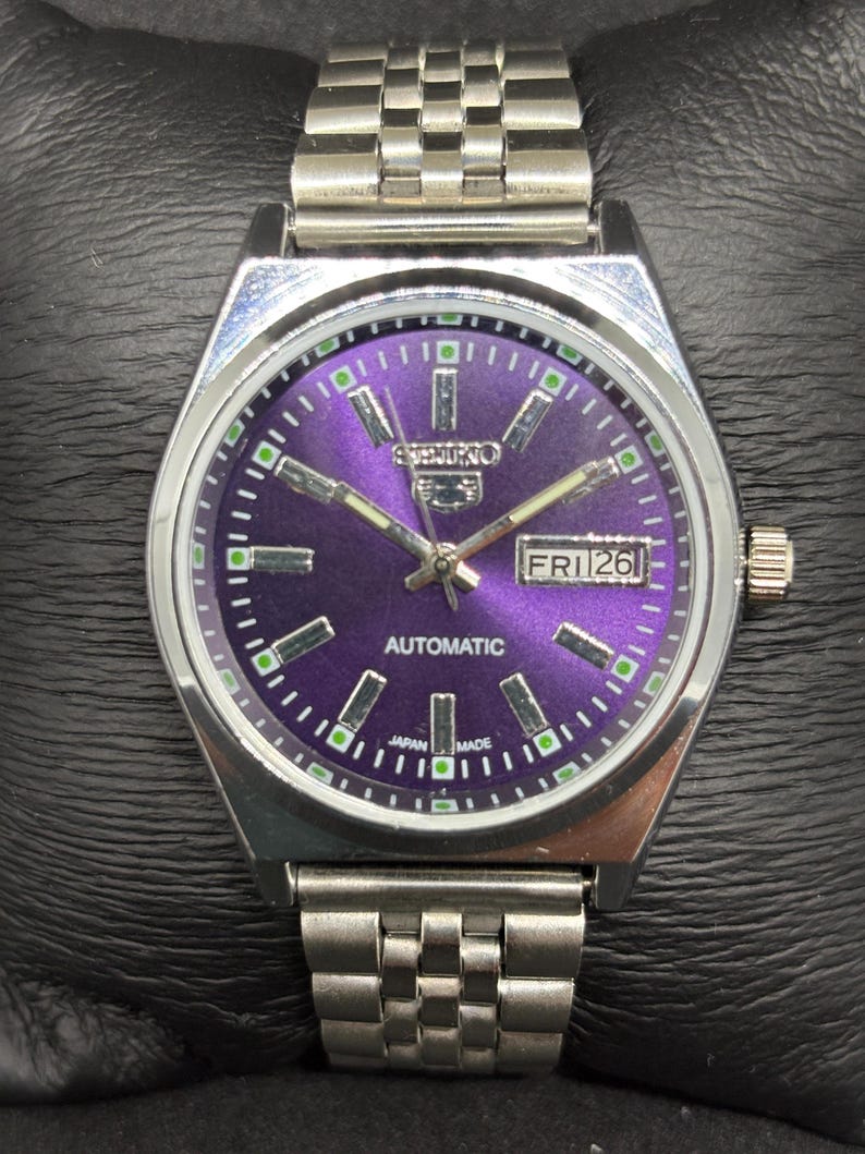 Peut inclure: Une montre-bracelet automatique en acier inoxydable argent&eacute; dot&eacute;e d'un cadran violet vif &agrave; effet soleil avec des index b&acirc;tons argent&eacute;s, des aiguilles luminescentes et un guichet jour-date &agrave; trois heures. Bracelet &agrave; maillons en m&eacute;tal.