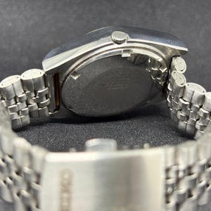 Peut inclure: Une montre-bracelet en acier inoxydable argent&eacute; avec un bo&icirc;tier rond et un bracelet en m&eacute;tal &agrave; maillons multiples. La montre comprend une petite couronne sur le c&ocirc;t&eacute; et un fermoir grav&eacute; du nom de la marque Seiko, montrant le dos du bo&icirc;tier.