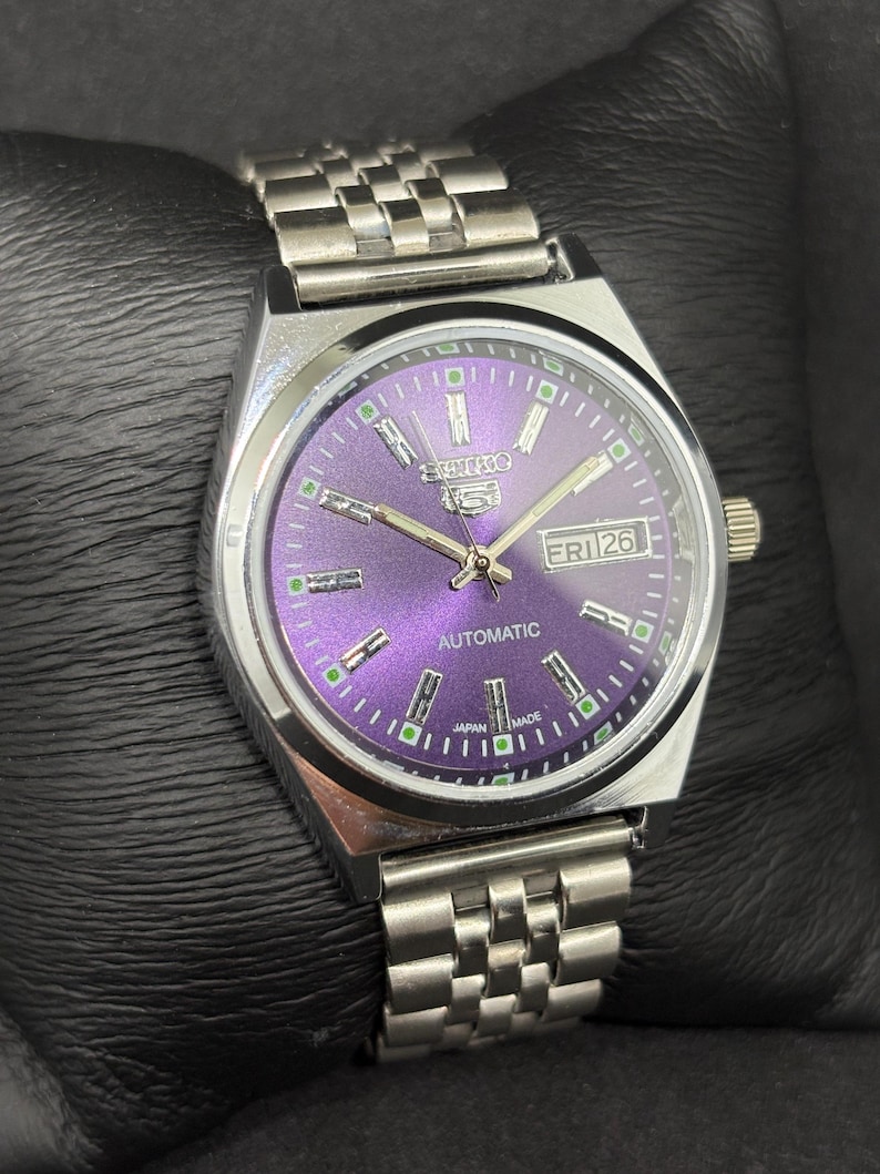 Peut inclure: Une montre automatique Seiko 5 en acier inoxydable dot&eacute;e d'un cadran violet &eacute;clatant, d'index argent&eacute;s avec des accents verts lumineux, d'un guichet jour-date &agrave; trois heures et d'un bracelet &agrave; maillons en m&eacute;tal argent&eacute; assorti.
