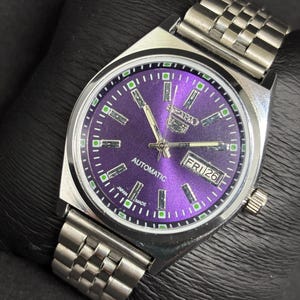 Peut inclure: Une montre-bracelet automatique Seiko 5 avec un cadran violet &eacute;clatant, des aiguilles argent&eacute;es et des index b&acirc;tons. La montre pr&eacute;sente un guichet jour-date &agrave; trois heures, un bo&icirc;tier en acier inoxydable et un bracelet &agrave; maillons assorti.