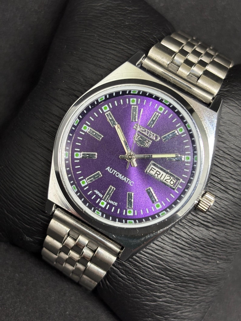 Peut inclure: Une montre-bracelet automatique Seiko 5 avec un cadran violet &eacute;clatant, des aiguilles argent&eacute;es et des index b&acirc;tons. La montre pr&eacute;sente un guichet jour-date &agrave; trois heures, un bo&icirc;tier en acier inoxydable et un bracelet &agrave; maillons assorti.