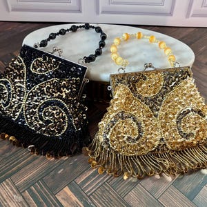 May include: Two beaded handbags with metal frames and clasp closures. One bag is black with gold sequin swirls and black fringe, featuring a black beaded handle. The other is gold with matching gold sequin swirls, fringe, and a yellow beaded handle.