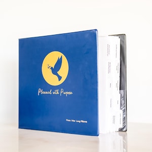 May include: A blue three-ring binder with a yellow circle logo featuring a bird holding a branch. The text reads Planned with Purpose and Cleo Mae Long Pillows. Inside are white tabbed dividers labeled with categories like Last Will and Testament.