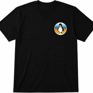 May include: A black short-sleeved t-shirt featuring a circular graphic on the upper left chest. The graphic depicts a black and white penguin with yellow feet and a yellow beak, set against a background of horizontal blue, orange, and yellow stripes.