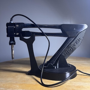 May include: A black articulated soldering iron stand with a circular base and a mechanical arm structure. The arm features the embossed text "CHAJUD" on its side. A black power cord is attached to the soldering iron held at the end of the arm.