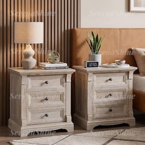 May include: Two light-toned wooden nightstands, each featuring three drawers with small dark round knobs. The nightstands have a rectangular top surface, a sturdy base with decorative molding, and a weathered finish showing wood grain texture.