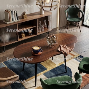 May include: A kidney-shaped dark walnut coffee table with thin black legs, featuring a blue ceramic mug with latte art on a wooden coaster, a geometric wire sculpture, and a folded tan napkin, set in a room with green chairs and a sideboard.