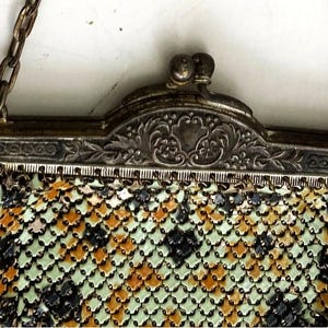 Peut inclure: Sac &agrave; main vintage en m&eacute;tal argent&eacute; avec une cha&icirc;ne. Le cadre est orn&eacute; de motifs floraux et de volutes. Le motif en r&eacute;sille pr&eacute;sente un m&eacute;lange de losanges noirs, orange et verts.