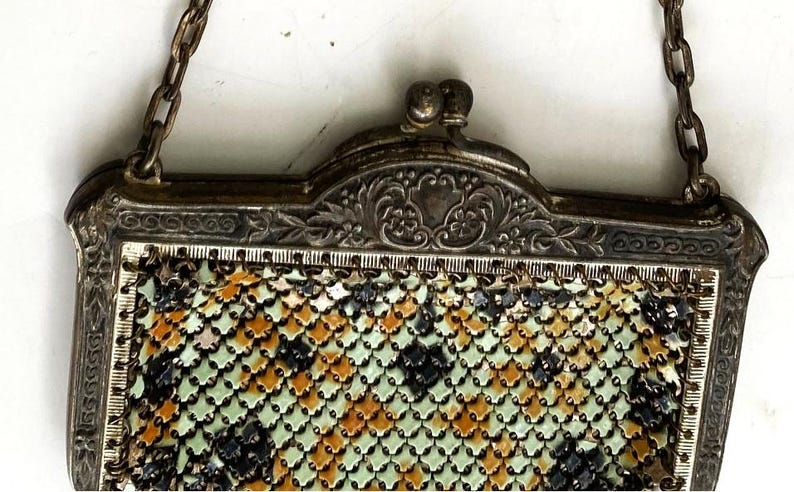 Peut inclure: Sac &agrave; main vintage en m&eacute;tal argent&eacute; avec une cha&icirc;ne. Le cadre est orn&eacute; de motifs floraux et de volutes. Le motif en r&eacute;sille pr&eacute;sente un m&eacute;lange de losanges noirs, orange et verts.