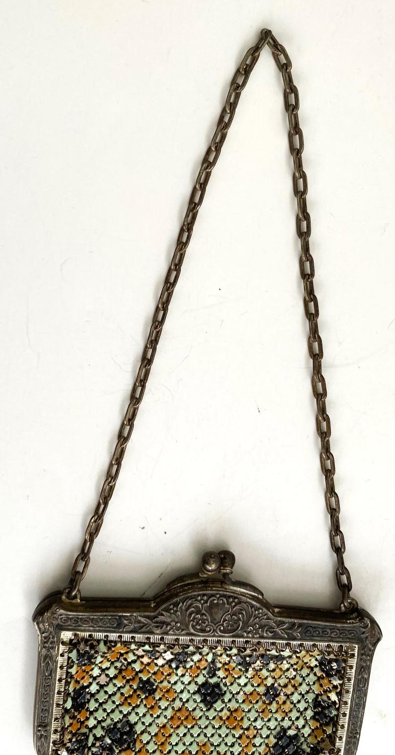 Peut inclure: Un sac &agrave; main ancien en m&eacute;tal argent&eacute; avec une cha&icirc;ne. Le sac pr&eacute;sente un cadre d&eacute;coratif avec des d&eacute;tails floraux et une fermeture &agrave; fermoir. Le motif en r&eacute;sille comprend des couleurs noires, vertes et oranges.