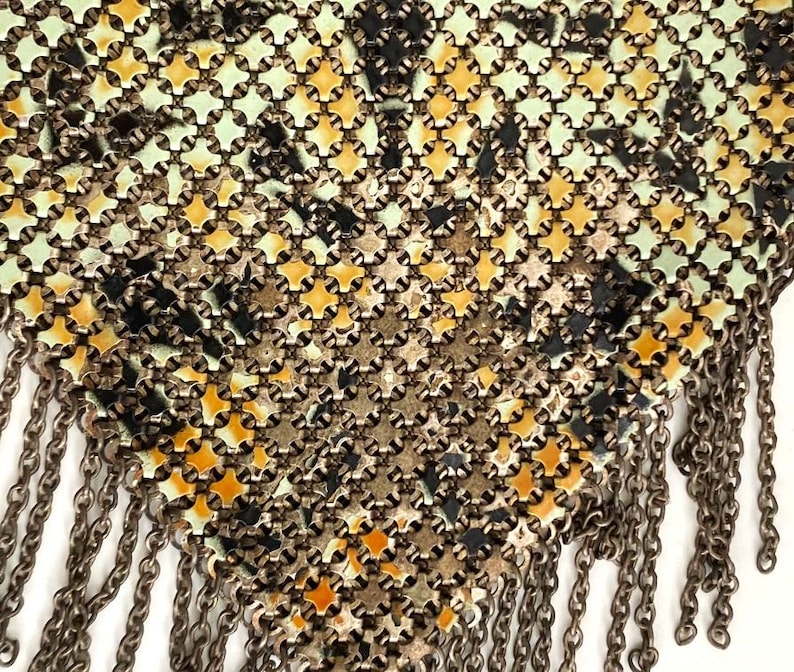 Peut inclure: Gros plan sur un sac &agrave; main vintage en m&eacute;tal maill&eacute; avec un motif g&eacute;om&eacute;trique dans les tons de vert, jaune, noir et argent. Le sac &agrave; main pr&eacute;sente une frange de cha&icirc;nes m&eacute;talliques pendantes sur le bord inf&eacute;rieur.