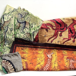 May include: Three pieces of fabric with distinct patterns. One features green and blue floral motifs, another displays red antelopes on a yellow honeycomb background, and the third shows giraffes in an orange and brown landscape with a dark border.