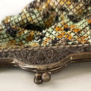 Peut inclure: Un sac &agrave; main ancien en m&eacute;tal maill&eacute; avec un cadre d&eacute;coratif argent&eacute;. Le sac pr&eacute;sente un motif color&eacute; de vert, orange et noir. Le cadre a des d&eacute;tails floraux orn&eacute;s et une fermeture &agrave; fermoir.