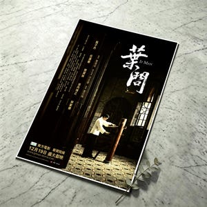 May include: A rectangular movie poster for Ip Man featuring a person in a white shirt practicing on a wooden dummy. The poster includes white Chinese calligraphy, the text Ip Man, and release information in the bottom left corner on a black background.