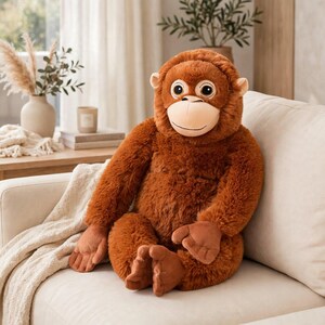 May include: A plush orangutan stuffed animal with long, shaggy, rust-colored fur, a smooth light beige face, and large dark eyes. The toy is seated in an upright position with long arms and legs, featuring soft, rounded hands and feet.