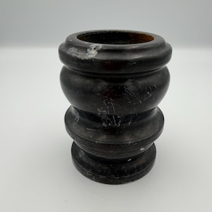 May include: A dark charcoal black stone vessel featuring a rounded, multi-tiered silhouette with a wide circular rim and a stable base. The polished surface displays natural white veining and subtle surface wear, creating a textured appearance.
