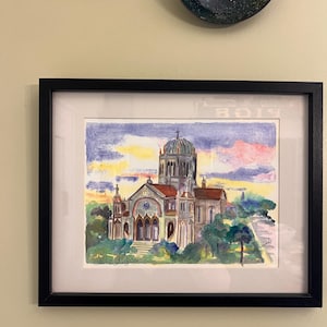 May include: A framed watercolor painting of a church with a central dome and a cross, set against a sunset sky with purple, yellow, and pink clouds. The building features arched windows and a red roof, with the text Saint Augustin written below.
