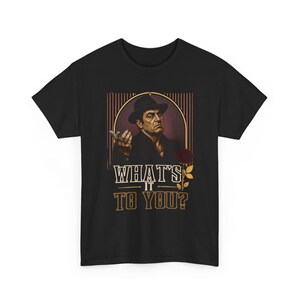 May include: A black short-sleeved t-shirt featuring a graphic print of a man in a dark hat and suit. The design includes a red rose and the text "WHAT'S IT TO YOU?" in a bold, light-coloured font, set against a background of vertical lines.