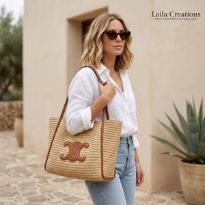 K&ouml;nnte beinhalten: Eine beige geflochtene Strohtasche mit braunem Lederbesatz und einem markanten braunen Lederlogo auf der Vorderseite. Die Tasche hat zwei Schulterriemen aus braunem Leder. Der Text Laila Creations Where Style Meets Everyday Carry ist in der oberen rechten Ecke zu sehen.