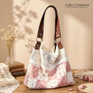 Peut inclure: Un sac à bandoulière de style hobo avec un motif patchwork en tissu floral rose et blanc. La partie supérieure est ornée d'une bordure en dentelle blanche. Il possède deux anses en cuir marron fixées par des anneaux et rivets dorés.