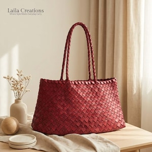 May include: A deep red tote bag featuring an intricate woven pattern throughout the body and two long braided shoulder straps. The bag displays the text Laila Creations Where Style Meets Everyday Carry in the upper left corner of the image.