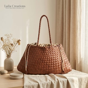 May include: A brown woven leather tote bag with two braided shoulder straps and a beige drawstring closure. The bag features a textured grid pattern and is branded with the text Laila Creations Where Style Meets Everyday Carry.