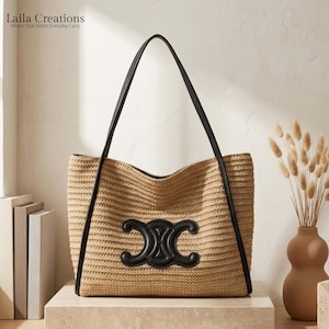 K&ouml;nnte beinhalten: Eine beigefarbene Tasche aus geflochtenem Stroh mit schwarzen Lederriemen und einem markanten schwarzen Lederemblem auf der Vorderseite. Der Text Laila Creations Where Style Meets Everyday Carry ist oben links im Bild zu sehen.