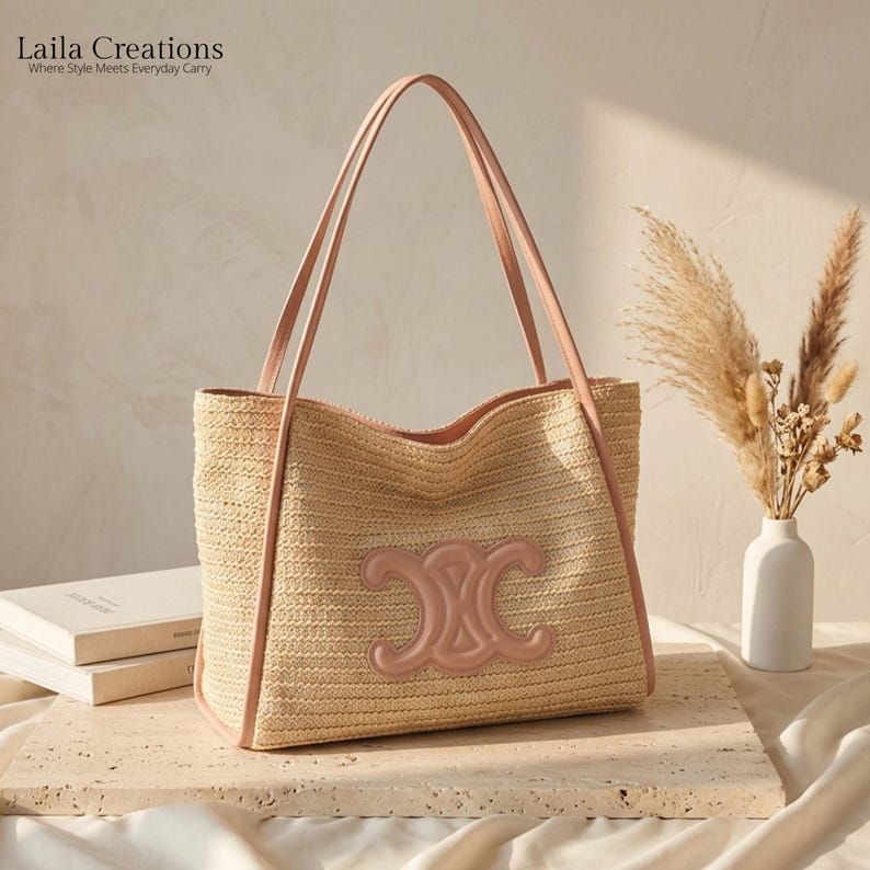 K&ouml;nnte beinhalten: Eine beige geflochtene Strohtasche mit zwei hellrosa Schulterriemen und einem passenden hellrosa gepr&auml;gten Logo-Emblem auf der Vorderseite. Der Text Laila Creations Where Style Meets Everyday Carry ist in der oberen linken Ecke zu sehen.