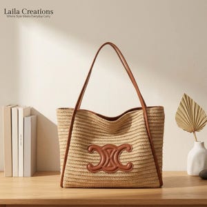 K&ouml;nnte beinhalten: Eine beige geflochtene Strohtasche mit braunen Leder-Schulterriemen und einem markanten braunen Lederemblem auf der Vorderseite. Die Tasche hat eine strukturierte rechteckige Form mit horizontalen Linien im geflochtenen Material.