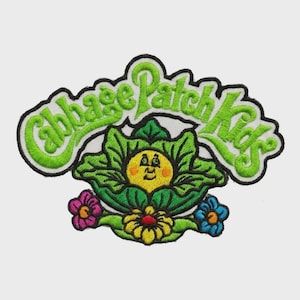 Könnte beinhalten: Ein gestickter Aufnäher mit dem Text Cabbage Patch Kids in leuchtend grünem Garn. Unter dem Text befindet sich ein gelbes, kreisförmiges Gesicht mit lächelndem Ausdruck, eingebettet in grüne Kohlblätter, flankiert von einer rosa und einer blauen Blume.