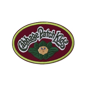 Könnte beinhalten: Ein ovaler, bestickter Aufnäher mit tief bordeauxrotem Hintergrund und einem hellen lindgrünen Rand. Der Schriftzug Cabbage Patch Kids ist in Weiß mit dunkelgrünen Umrandungen über einem kleinen, beigen Gesicht eines Wesens in grünen Blättern gestickt.